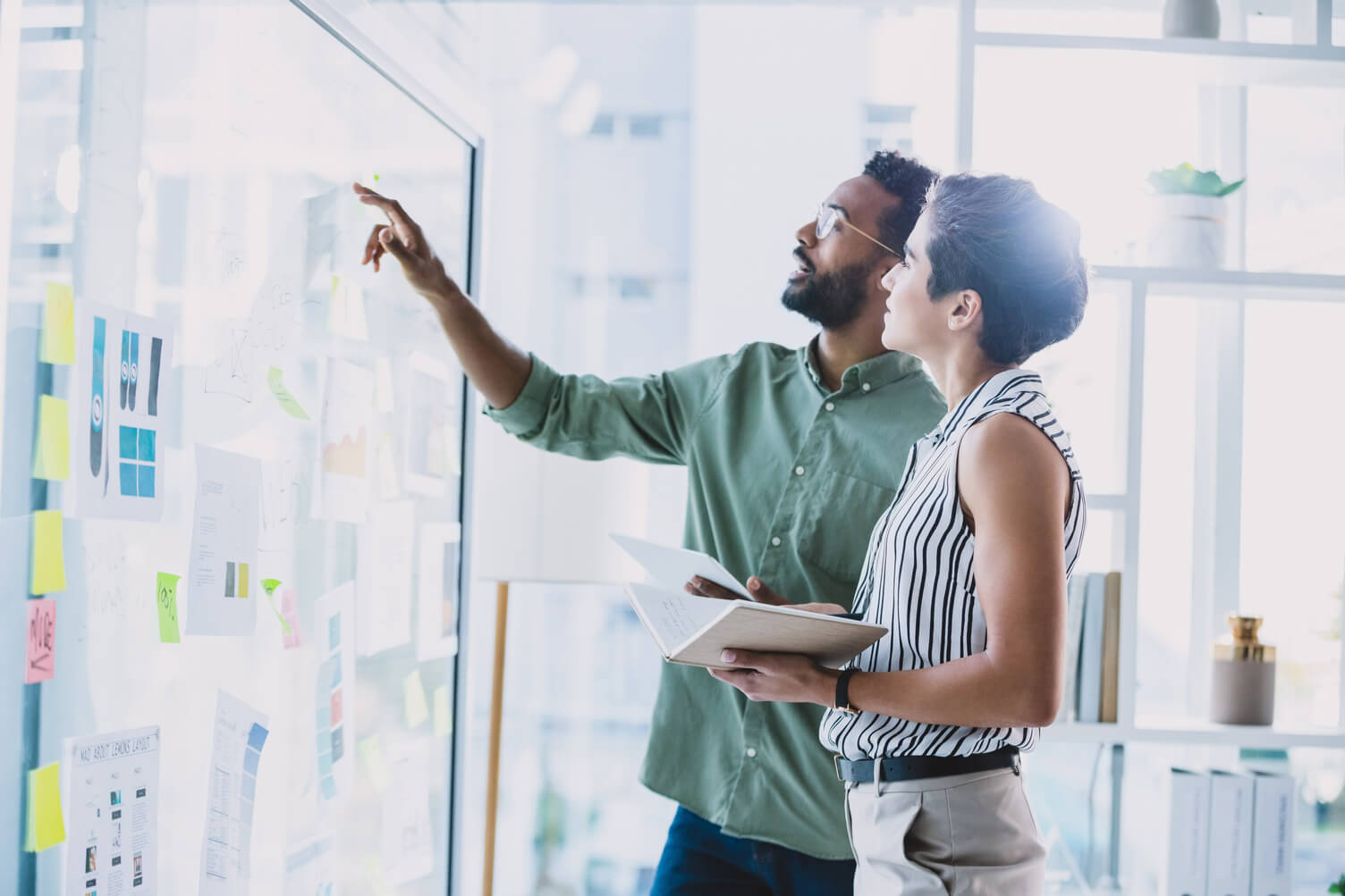 Two colleagues looking at sticky notes on a whiteboard