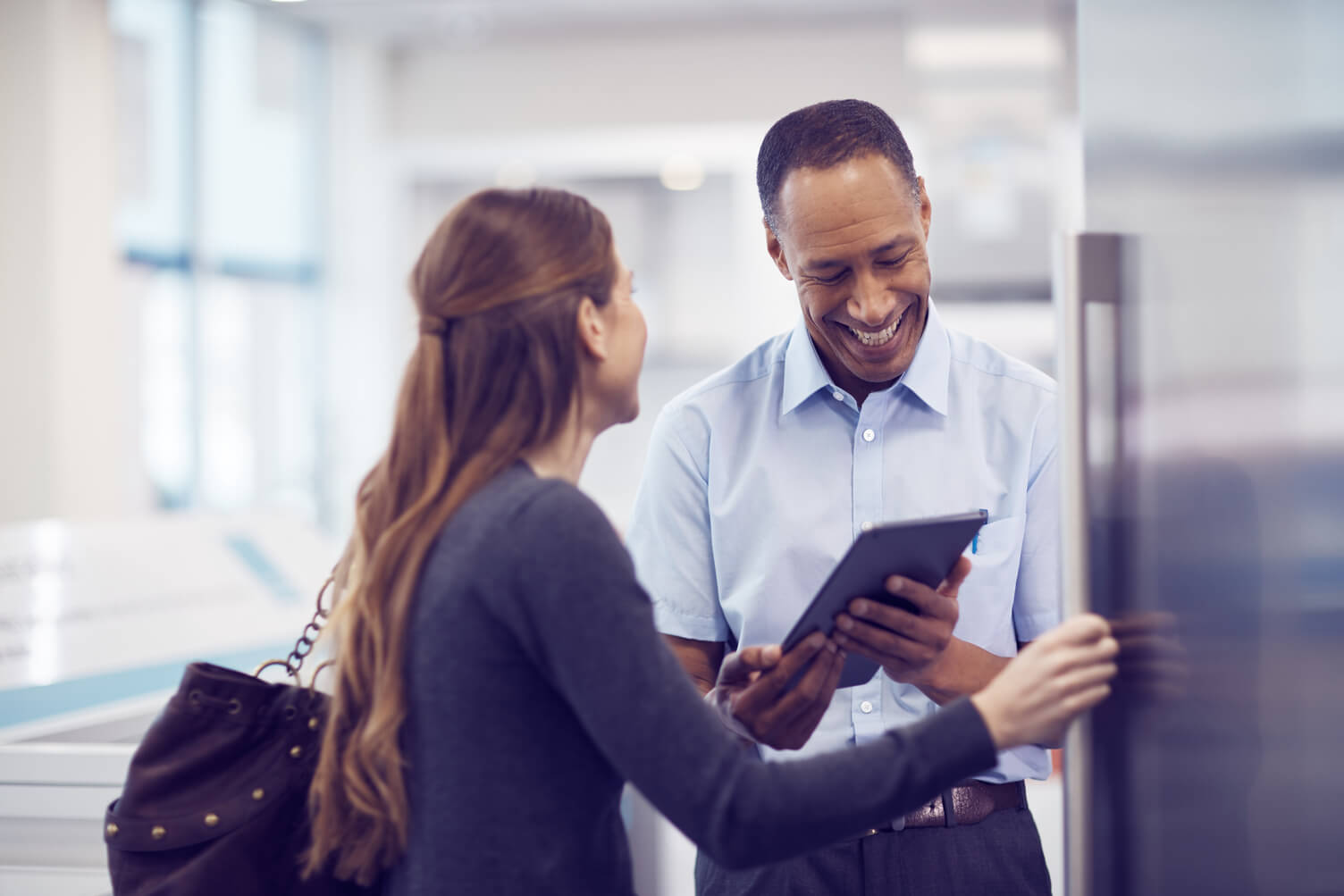 A man and woman at work smiling the man has a tablet in his hands