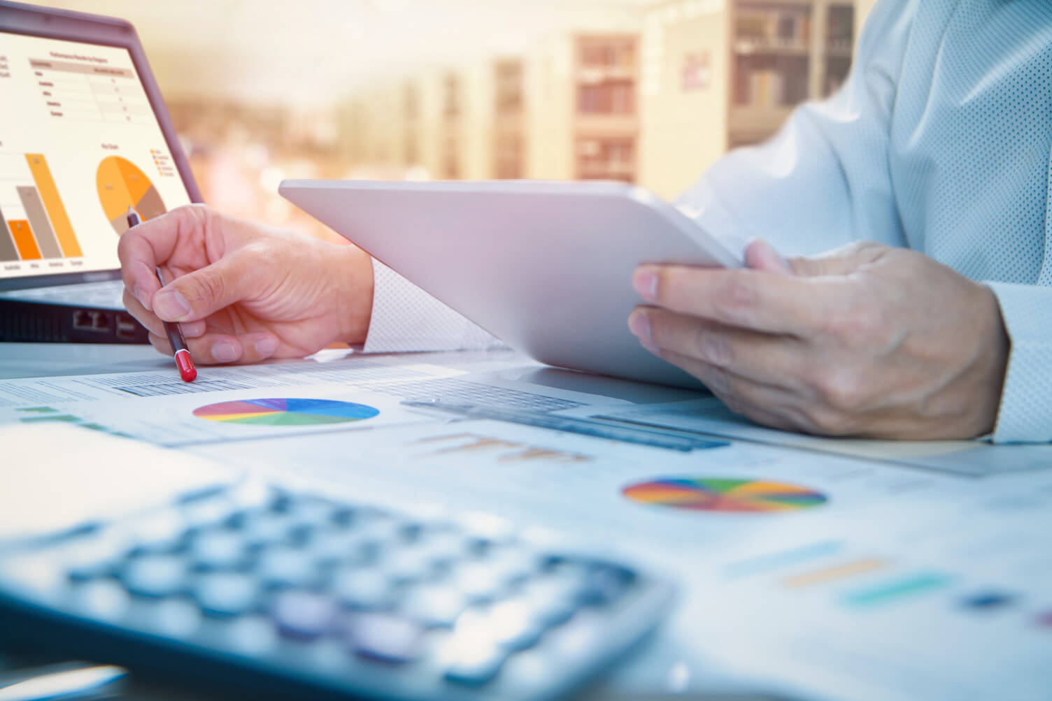 close up image of a mans hands holding paper next to a laptop and calculator