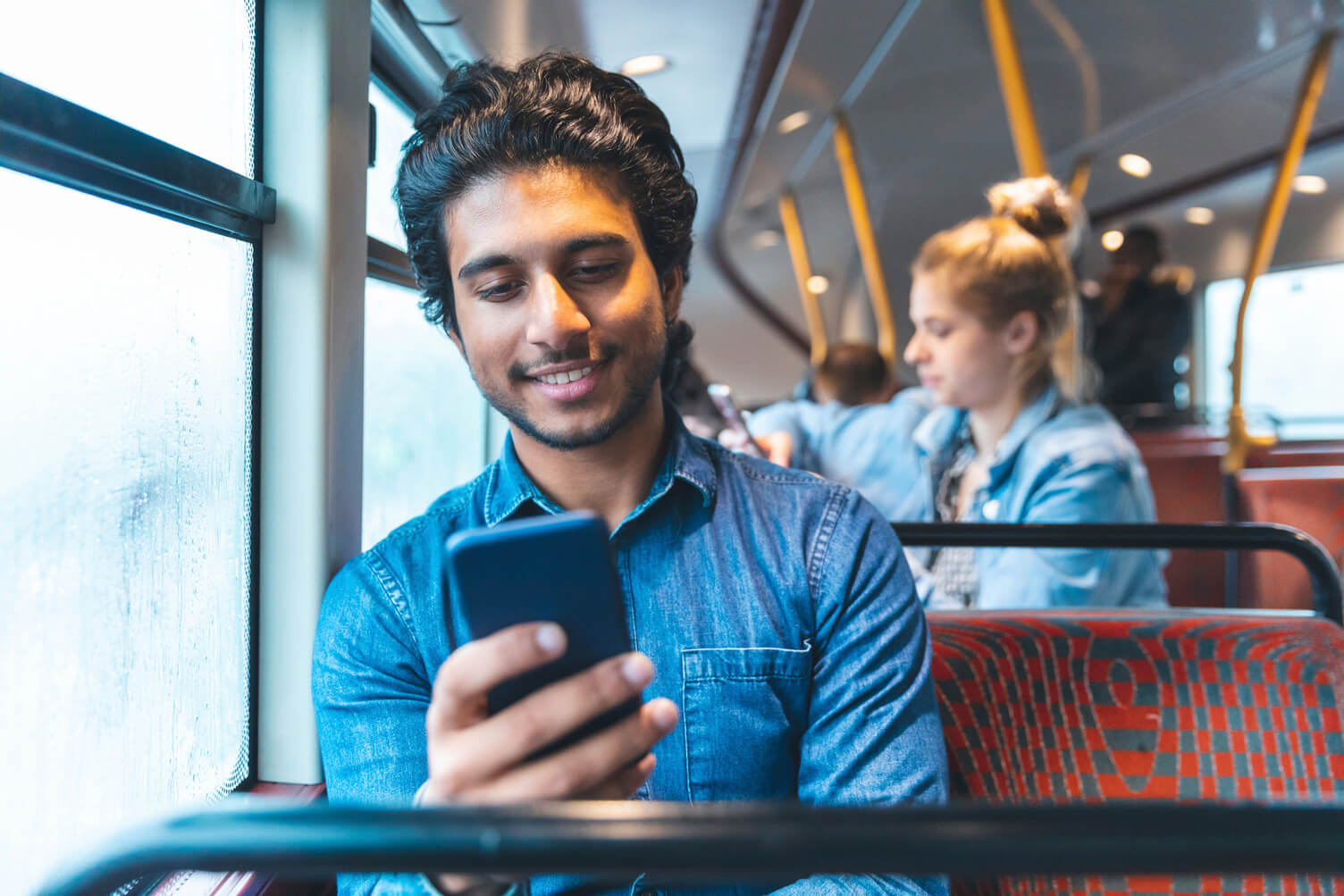 Man smiling while looking his phone on a bus