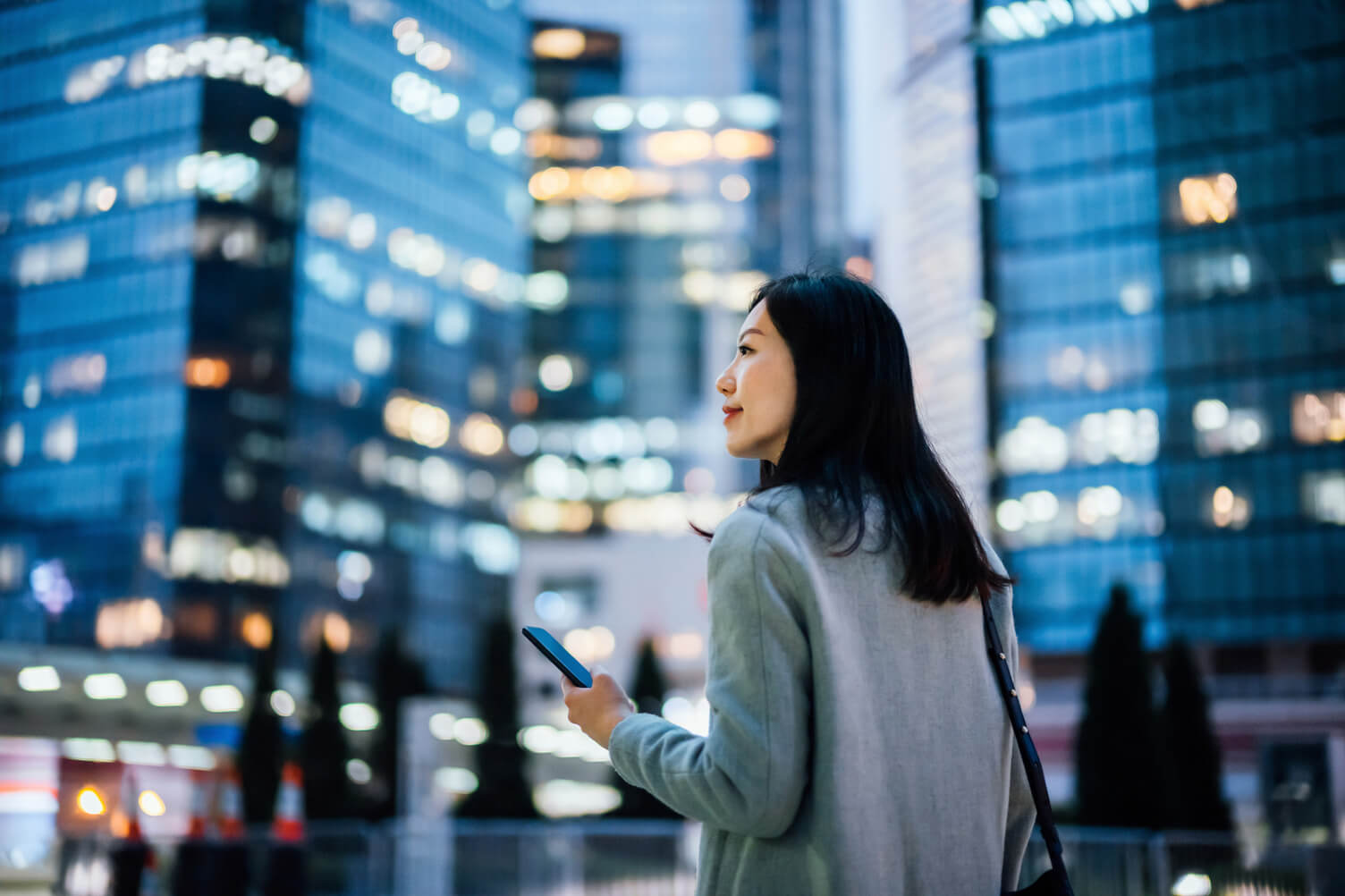 a women with a phone in her hand walking with a city in the background