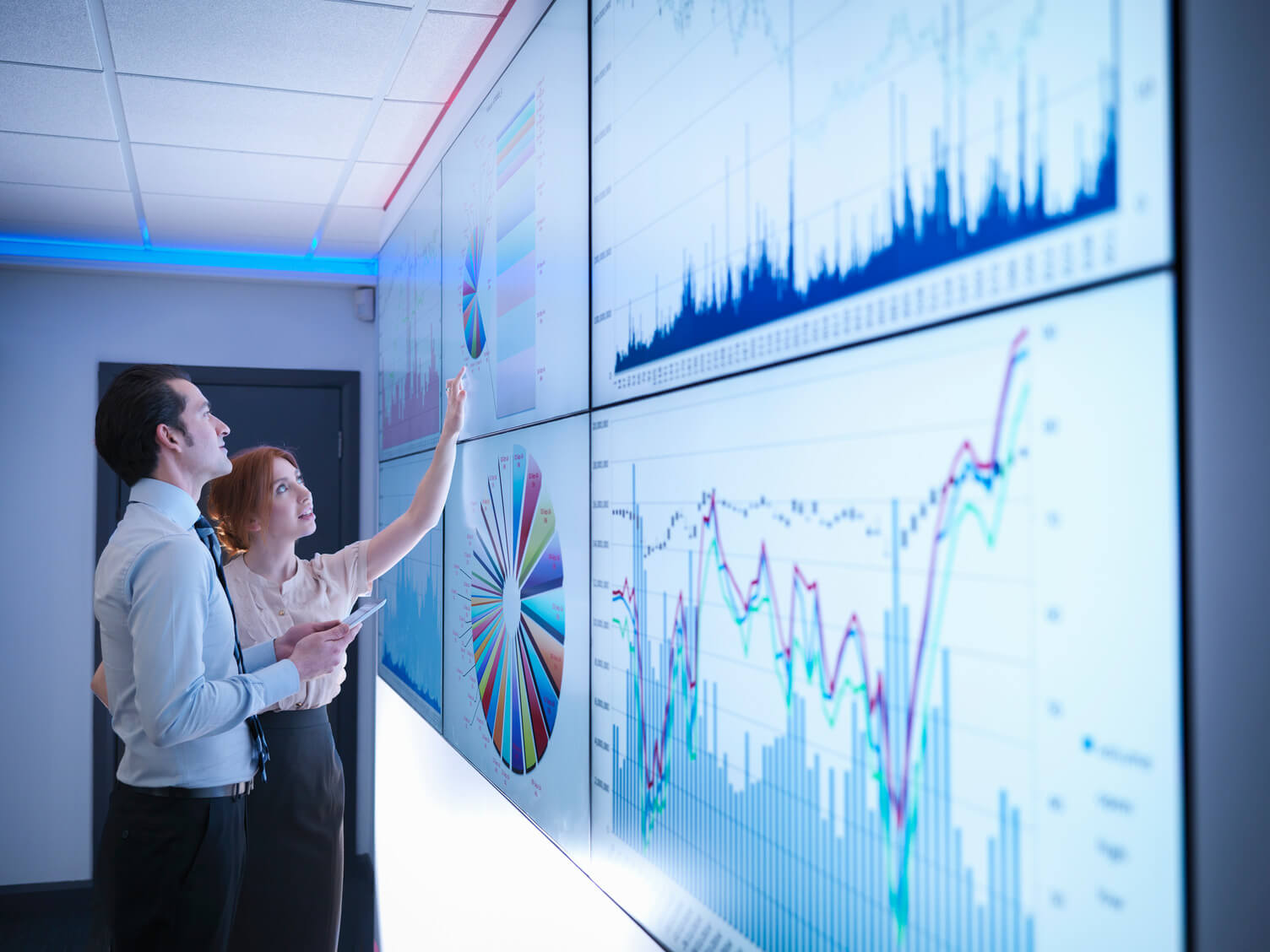 a man and a woman looking at a large screen showing data graphs