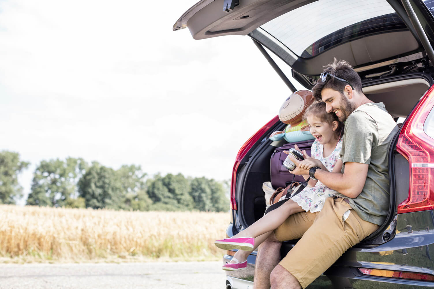Father and his daughter sat outside the car while playing
